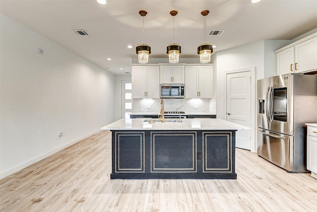 kitchen with stainless steel appliances, decorative light fixtures, a kitchen island with sink, and white cabinets