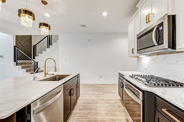 kitchen with sink, hanging light fixtures, light wood-type flooring, appliances with stainless steel finishes, and white cabinets