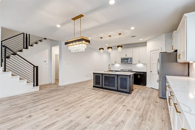 kitchen with pendant lighting, sink, appliances with stainless steel finishes, white cabinetry, and a center island with sink