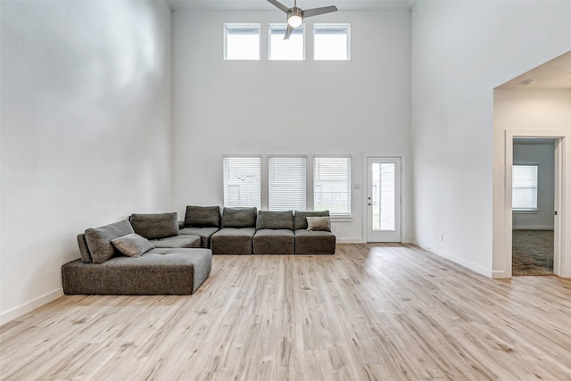 living room with ceiling fan, a towering ceiling, and light wood-type flooring