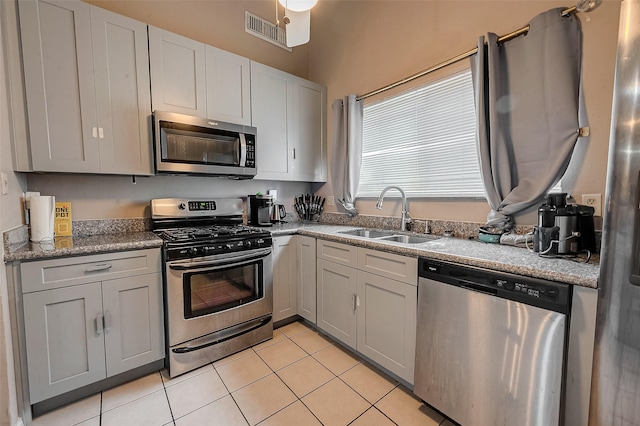 kitchen featuring sink, gray cabinetry, stone countertops, light tile patterned floors, and stainless steel appliances