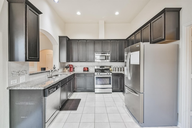 kitchen with sink, light stone counters, light tile patterned floors, appliances with stainless steel finishes, and decorative backsplash