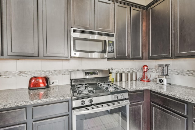 kitchen featuring backsplash, dark brown cabinets, stainless steel appliances, and light stone countertops