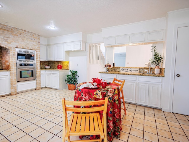 kitchen with appliances with stainless steel finishes, white cabinetry, light stone countertops, light tile patterned flooring, and decorative backsplash