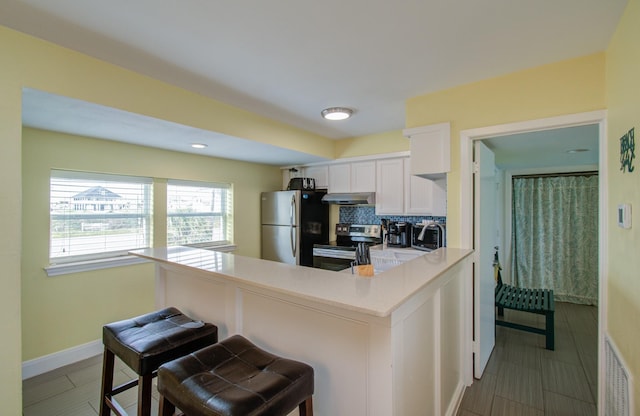 kitchen with a kitchen bar, appliances with stainless steel finishes, kitchen peninsula, decorative backsplash, and white cabinets