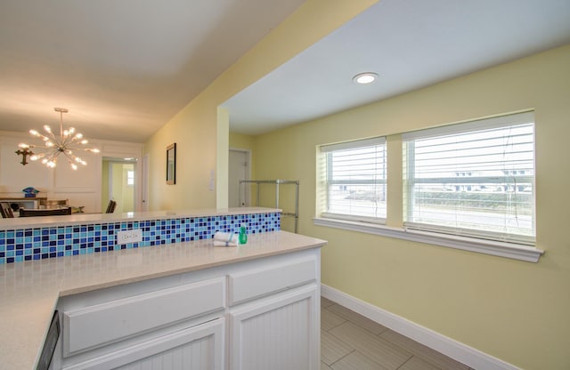 kitchen with pendant lighting, white cabinets, backsplash, light tile patterned floors, and a notable chandelier