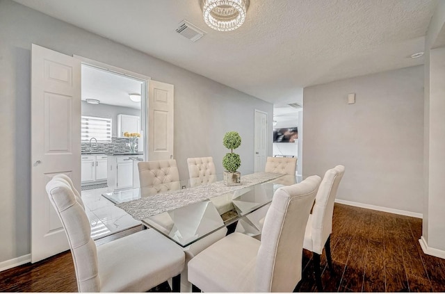 dining area featuring dark wood-type flooring, visible vents, a textured ceiling, and baseboards