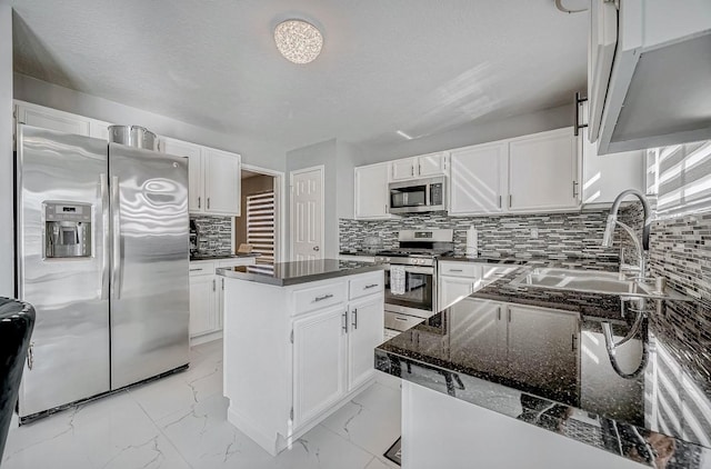 kitchen with dark stone counters, decorative backsplash, a sink, appliances with stainless steel finishes, and a center island