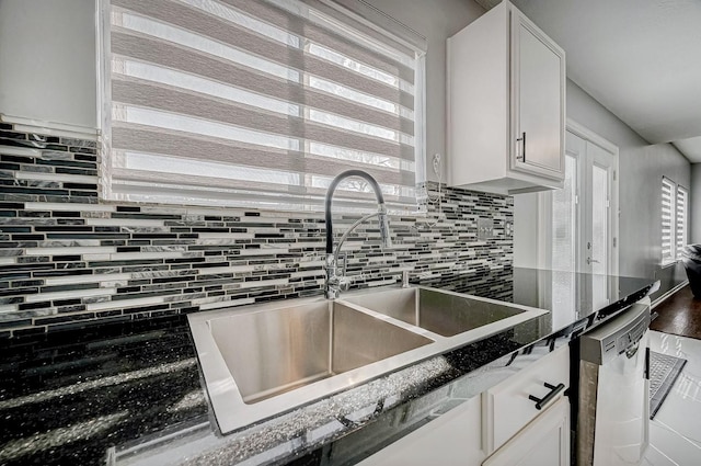 kitchen featuring dark stone countertops, stainless steel dishwasher, decorative backsplash, white cabinets, and a sink