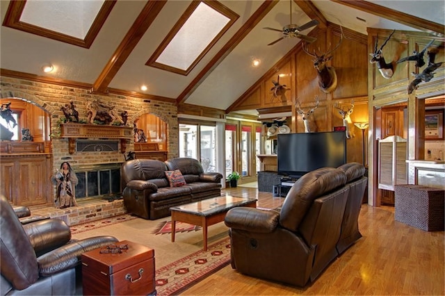 living room featuring high vaulted ceiling, a fireplace, a skylight, light hardwood / wood-style floors, and beam ceiling