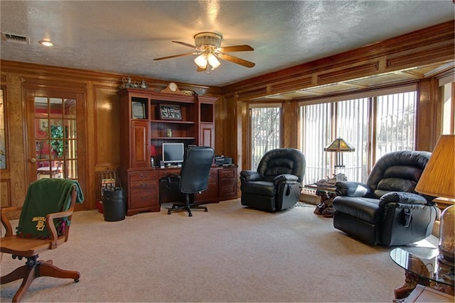 carpeted office space featuring ceiling fan, wooden walls, and a textured ceiling