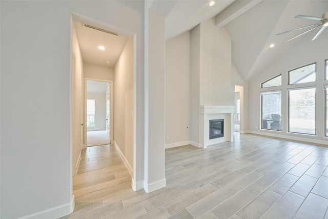 unfurnished living room with visible vents, a ceiling fan, a glass covered fireplace, light wood-type flooring, and beamed ceiling