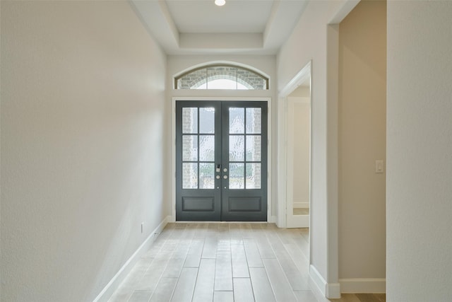 entryway with light wood finished floors, french doors, a raised ceiling, and baseboards