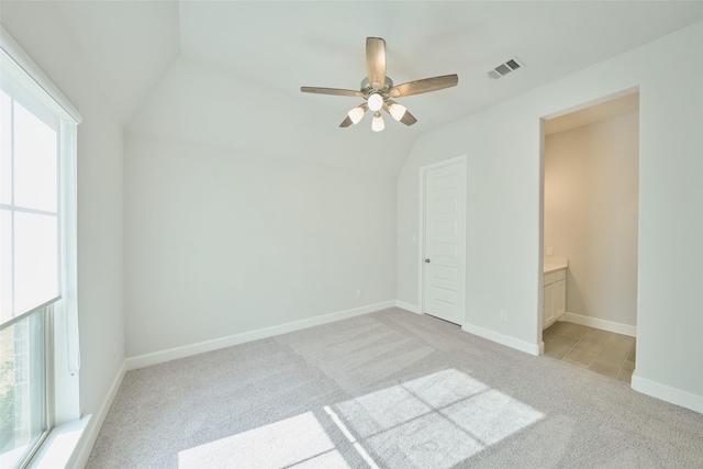 unfurnished bedroom with light carpet, baseboards, visible vents, lofted ceiling, and ensuite bath