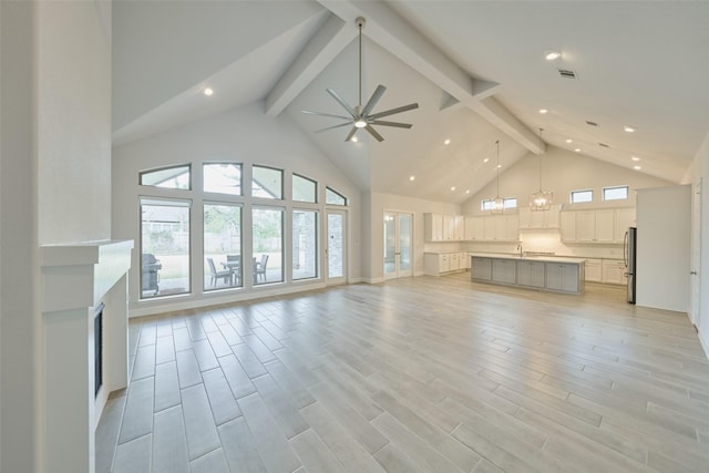 unfurnished living room featuring ceiling fan with notable chandelier, light wood-style floors, high vaulted ceiling, beam ceiling, and recessed lighting