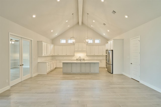 kitchen featuring a center island with sink, light countertops, hanging light fixtures, freestanding refrigerator, and white cabinetry