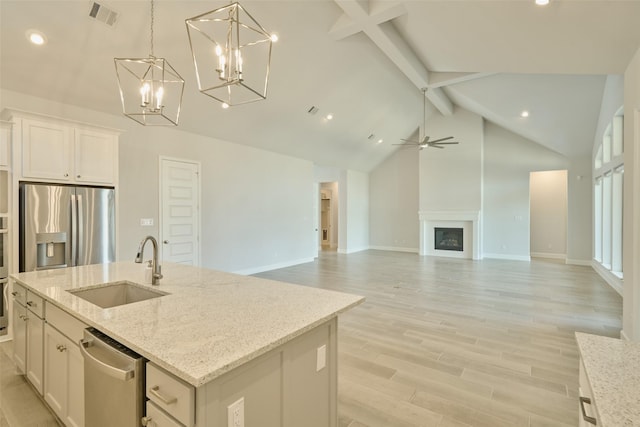 kitchen featuring appliances with stainless steel finishes, open floor plan, a kitchen island with sink, a sink, and white cabinetry