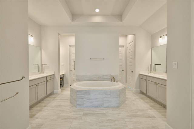 bathroom with baseboards, two vanities, a bath, and a raised ceiling