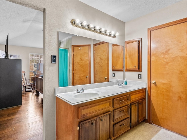 full bathroom with lofted ceiling, hardwood / wood-style floors, a textured ceiling, and a sink