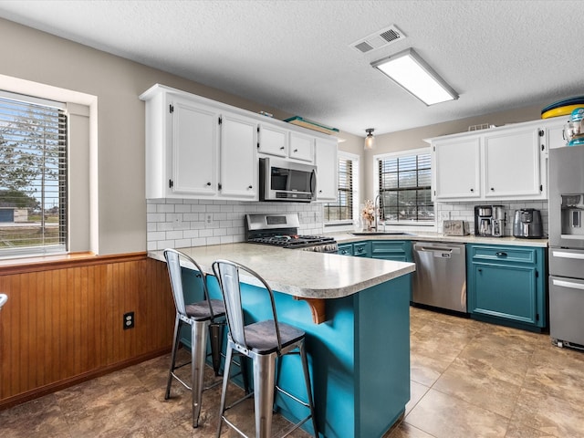 kitchen featuring visible vents, appliances with stainless steel finishes, a sink, wooden walls, and blue cabinets