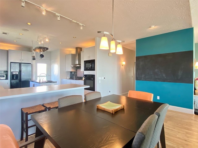 dining area featuring light wood-type flooring, sink, and a textured ceiling