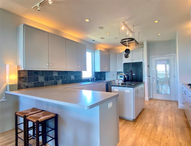 kitchen featuring a center island with sink, light wood-type flooring, a breakfast bar, and black refrigerator with ice dispenser