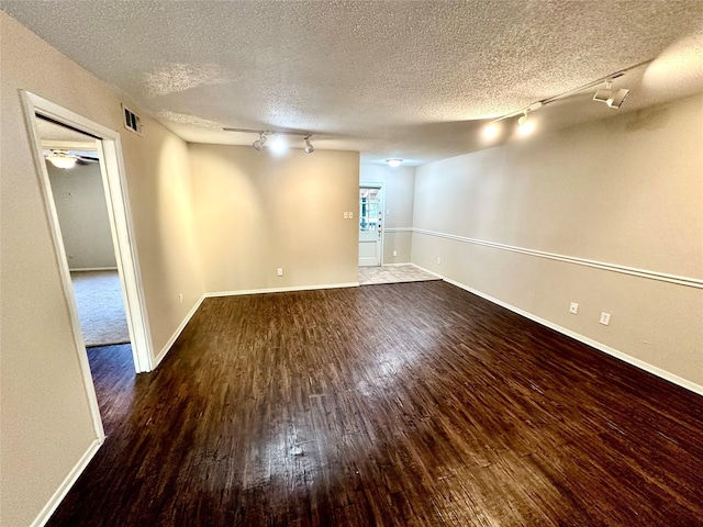 empty room featuring track lighting, a textured ceiling, and dark hardwood / wood-style flooring