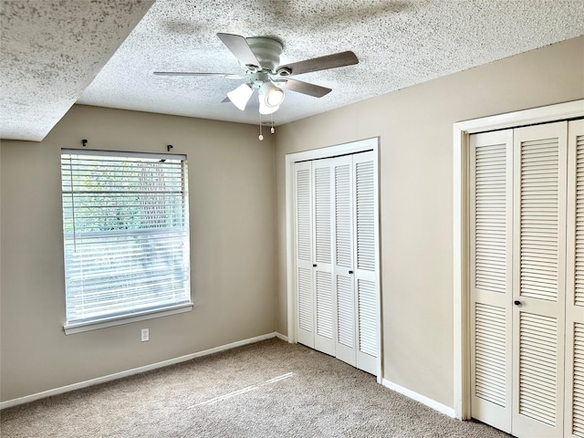 unfurnished bedroom with ceiling fan, two closets, a textured ceiling, and carpet