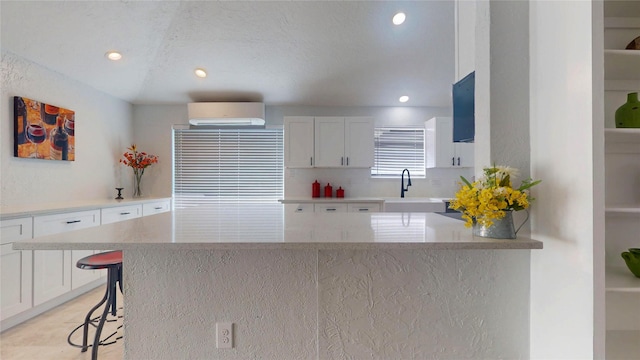 kitchen featuring sink, a breakfast bar, white cabinetry, a center island, and a wall mounted AC