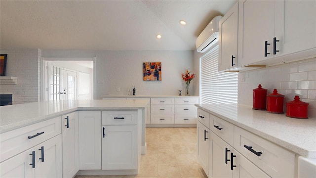 kitchen featuring white cabinetry, a wall unit AC, light stone counters, tasteful backsplash, and vaulted ceiling