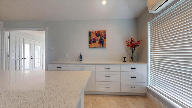 kitchen featuring light stone countertops, a wall mounted AC, and white cabinets