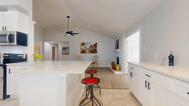 kitchen with vaulted ceiling, appliances with stainless steel finishes, a fireplace, white cabinets, and a kitchen breakfast bar