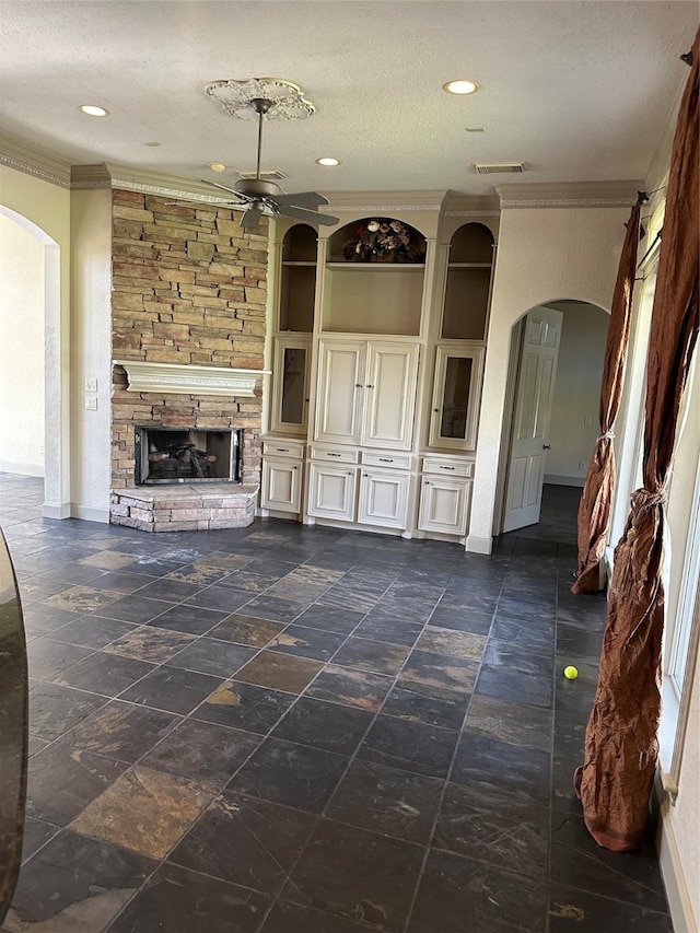 unfurnished living room with a stone fireplace, ornamental molding, ceiling fan, and a textured ceiling