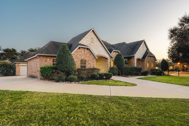 french country inspired facade featuring a garage and a lawn