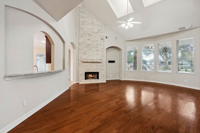 unfurnished living room with a skylight, high vaulted ceiling, hardwood / wood-style flooring, ceiling fan, and a fireplace