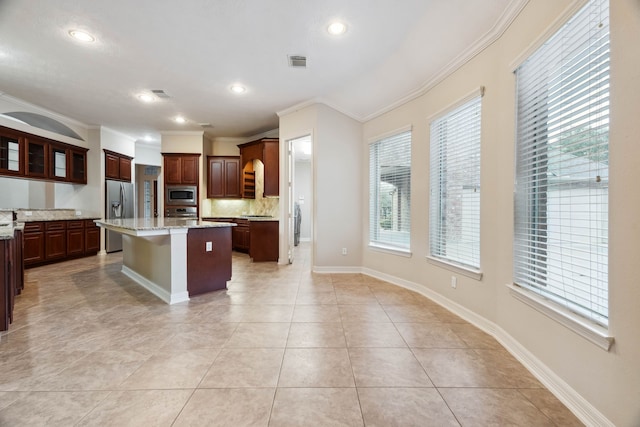 kitchen with crown molding, appliances with stainless steel finishes, a center island, a kitchen bar, and light tile patterned flooring