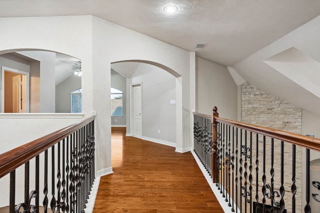 hallway with hardwood / wood-style flooring, vaulted ceiling, and a textured ceiling