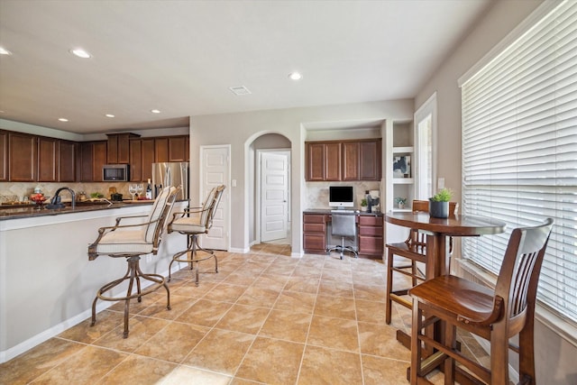 kitchen featuring a kitchen bar, appliances with stainless steel finishes, sink, light tile patterned floors, and decorative backsplash