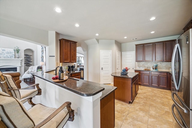 kitchen featuring a center island, stainless steel fridge, backsplash, a kitchen bar, and kitchen peninsula