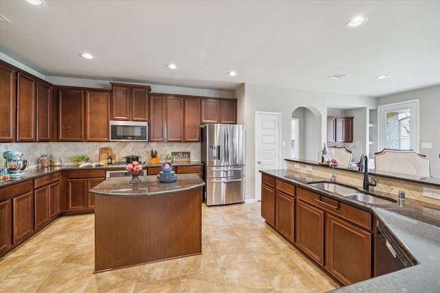 kitchen with a kitchen island, sink, dark stone counters, appliances with stainless steel finishes, and decorative backsplash