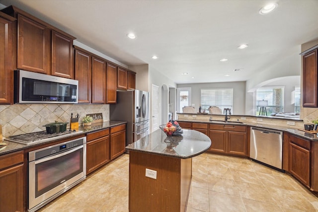 kitchen featuring dark stone countertops, sink, a kitchen island, stainless steel appliances, and kitchen peninsula