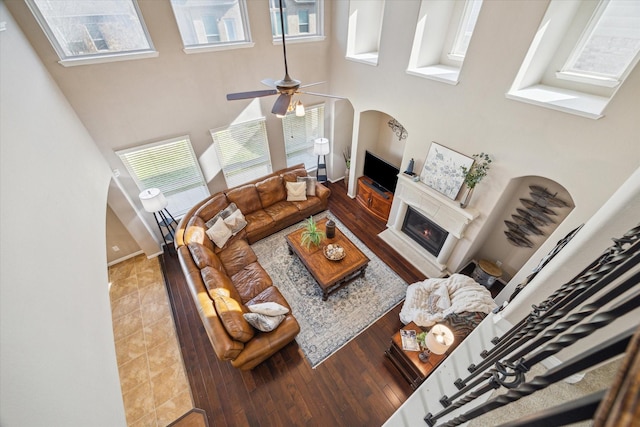 living room with ceiling fan, plenty of natural light, wood-type flooring, and a towering ceiling