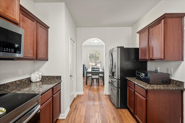 kitchen featuring appliances with stainless steel finishes, light hardwood / wood-style flooring, and dark stone counters