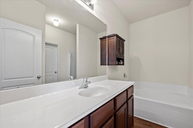 bathroom featuring hardwood / wood-style flooring, vanity, and tiled bath