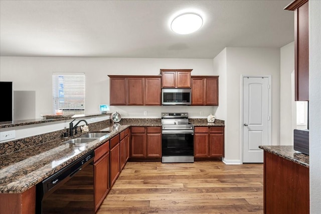 kitchen with sink, dark stone countertops, stainless steel appliances, light hardwood / wood-style floors, and kitchen peninsula