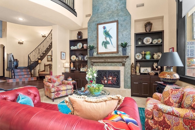 living room featuring light tile patterned floors, a high end fireplace, built in features, and a high ceiling