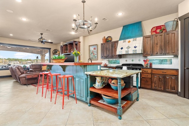 kitchen featuring tasteful backsplash, a breakfast bar area, hanging light fixtures, high end stainless steel range, and wall chimney range hood