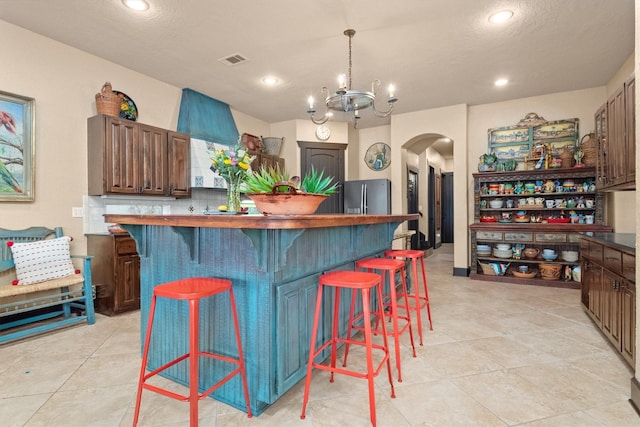 kitchen with stainless steel refrigerator with ice dispenser, dark brown cabinetry, a kitchen bar, a center island, and a chandelier