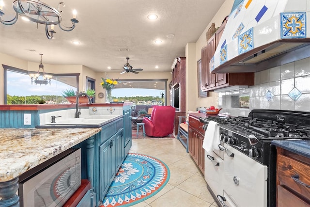 kitchen with range hood, light tile patterned floors, light stone countertops, ceiling fan with notable chandelier, and decorative backsplash