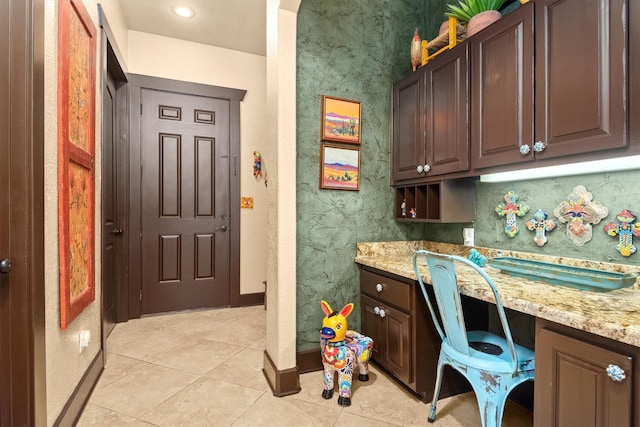 kitchen with dark brown cabinetry, built in desk, and light stone countertops